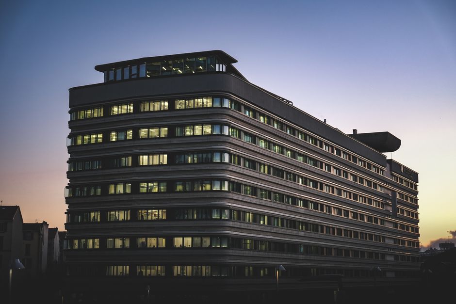 A modern office building beautifully illuminated against the twilight sky in an urban setting.