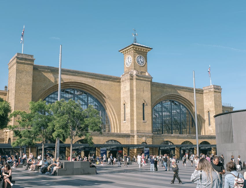 Sunny day at King's Cross Station, London, capturing the historic clock tower and bustling plaza.